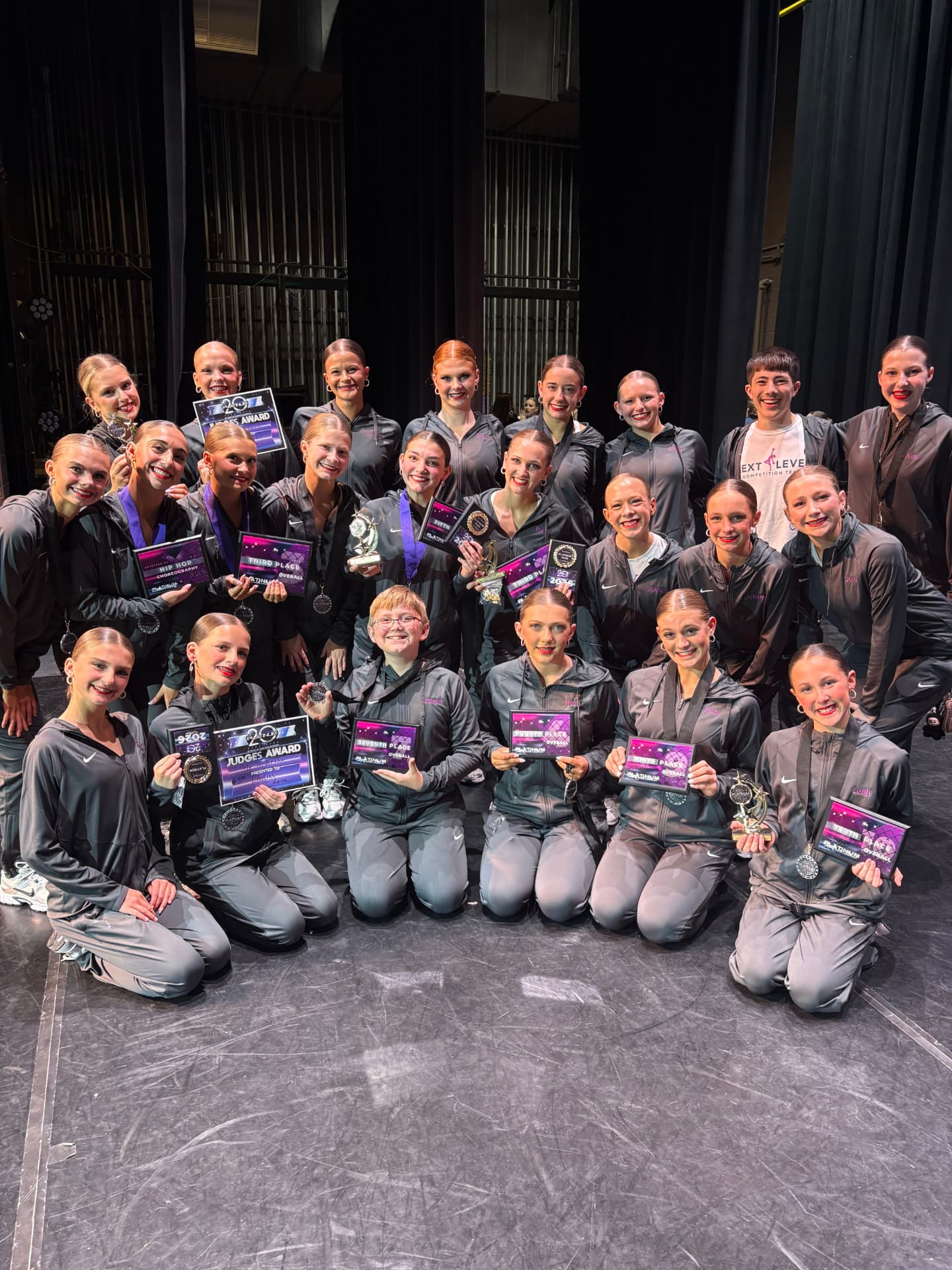 Next Level dancers holding platinum awards and medals on stage