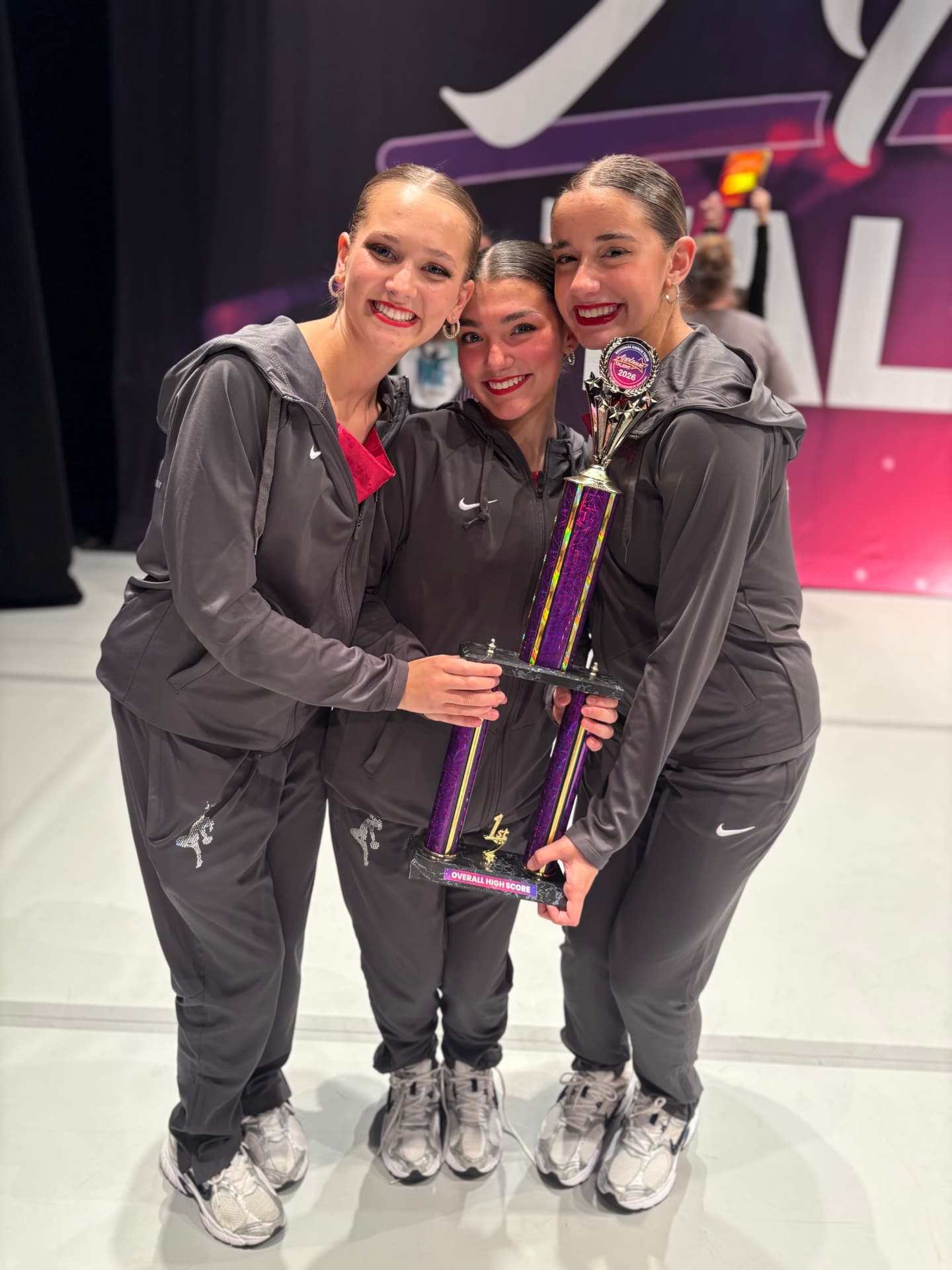Three Next Level dancers hugging with a first place trophy