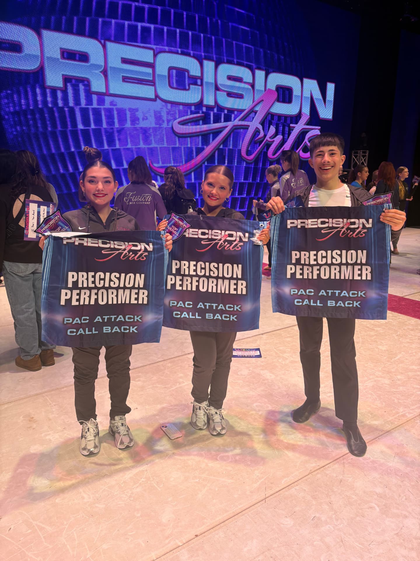 Three Next Level dancers holding Precision Performer PAC Attack callback banners